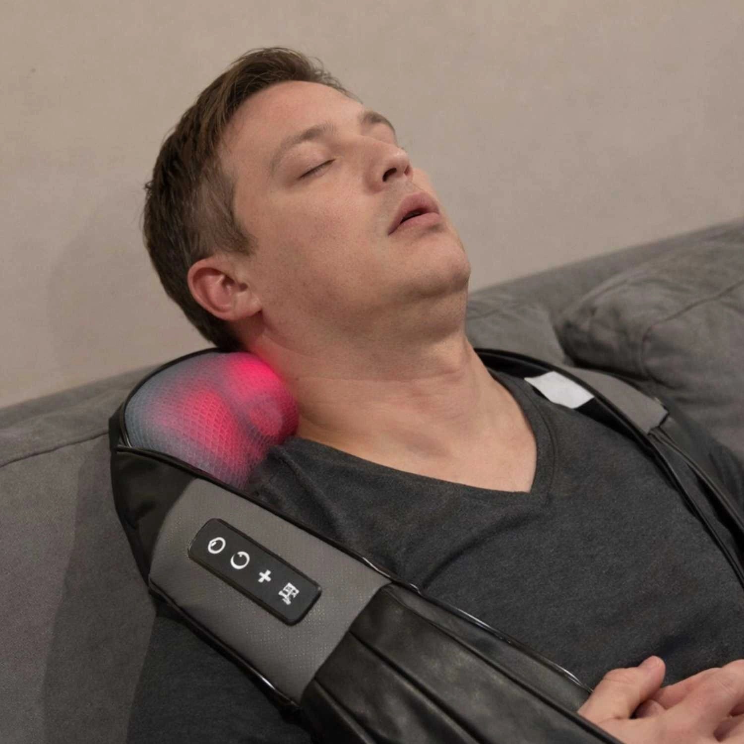 Man receiving neck massage from a handheld device with red light on a gray couch.